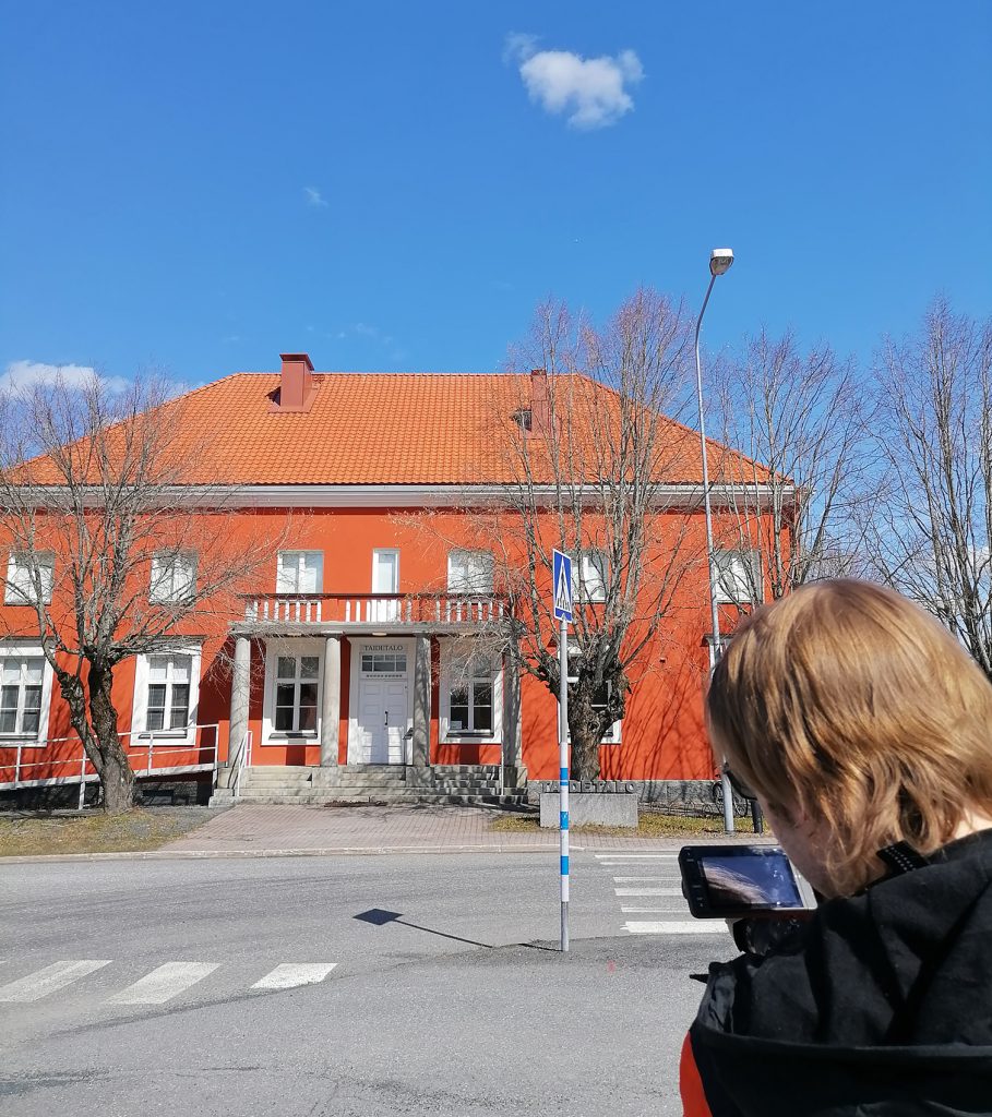 Tiimin jäsen Eetu etualalla kuvaamassa punertavaa rakennusta (Loimaan Taidetaloa).